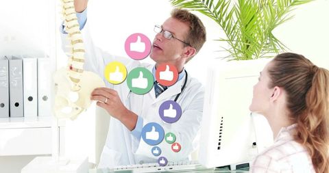 Doctor explaining spine anatomy to patient during consultation with thumbs-up icons