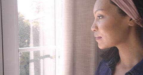 Woman Gazing Thoughtfully Through Sunlit Window at Home