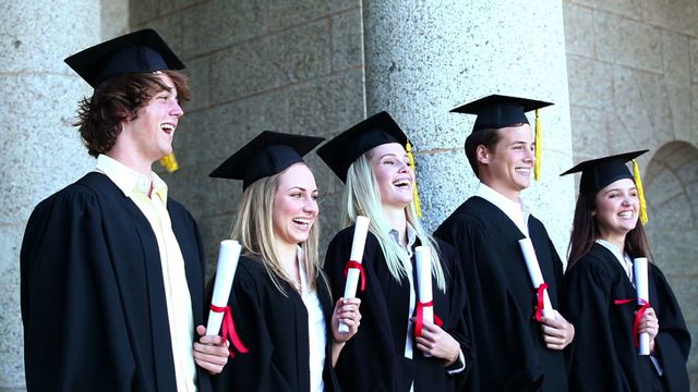 Group of happy young graduates celebrating their commencement ceremony. They wear traditional caps and gowns while holding their diplomas. This concept is ideal for illustrating success, achievement, and academic accomplishment. Perfect for educational websites, university brochures, and articles about student success.