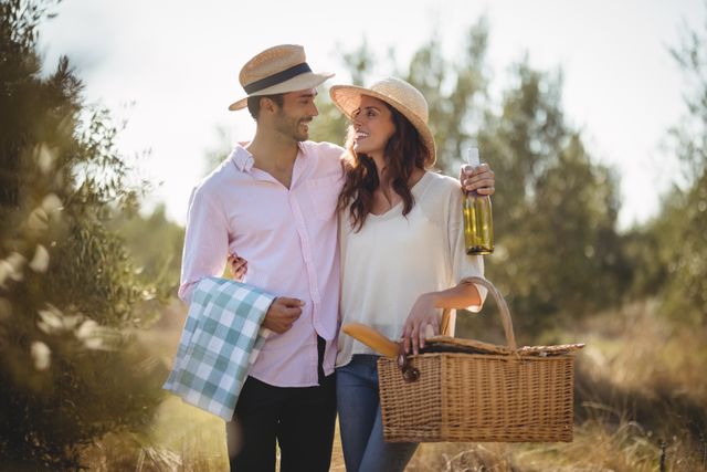 Happy young couple looking at each other while carrying picnic basket at olive farm