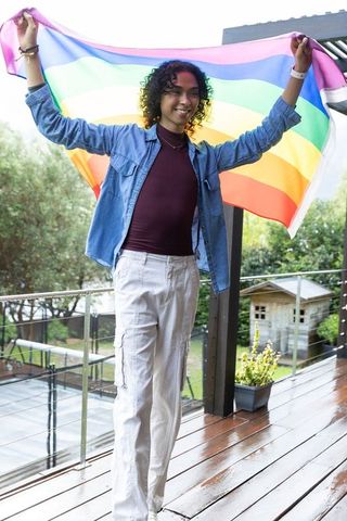 Non-binary holding rainbow pride flag on wet deck celebrating lgbtq inclusion