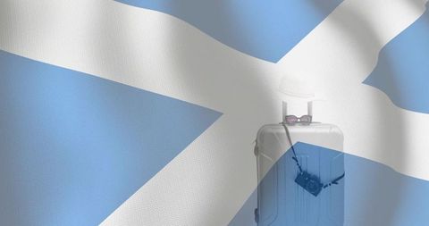 Silver suitcase with straw hat, sunglasses and camera on scottish saltire for travel concept