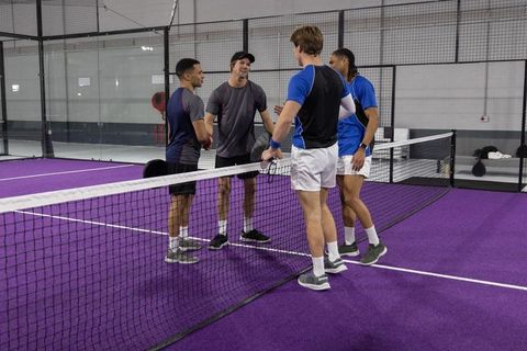 Four male players shaking hands on purple indoor racket court showing sportsmanship