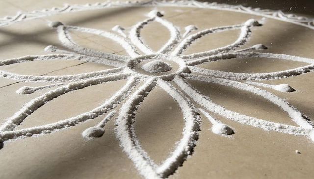 Creating white powder mandala with eight-petal floral loops on beige floor emphasizing texture and s