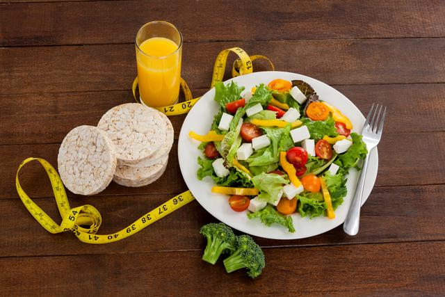 Salad, juice, edible bars and measuring tape on table - diet concept