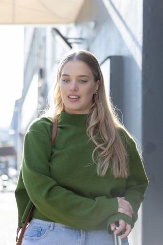 Backlit young woman walking urban sidewalk wearing green sweater and denim holding handrail