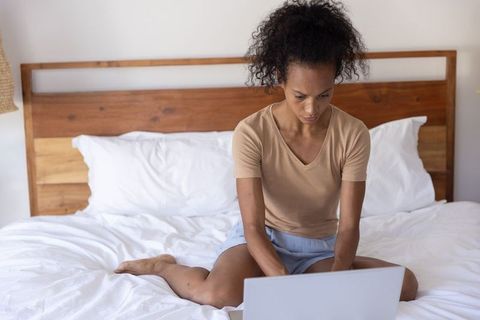 African american woman working on laptop on bed studying for online class and remote work