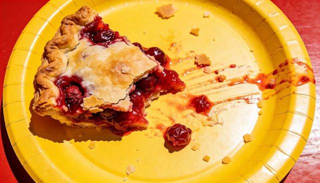 Sunlit half-eaten cherry pie slice on yellow plate with glossy filling and crumbs