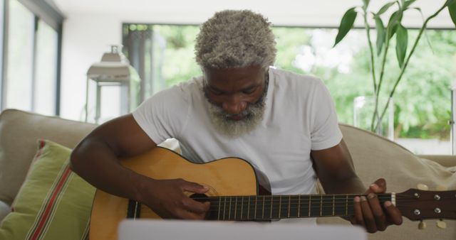 Image of sad african american senior man playing the guitar and using laptop - Download Free Stock Photos Pikwizard.com