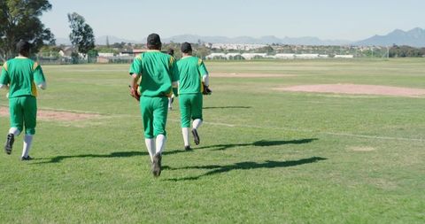 Baseball Teammates Running Across Outfield in Green Uniforms Carrying Gloves and Caps