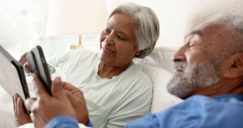 Smiling Senior Couple Using Tablets and Smartphones in Bed