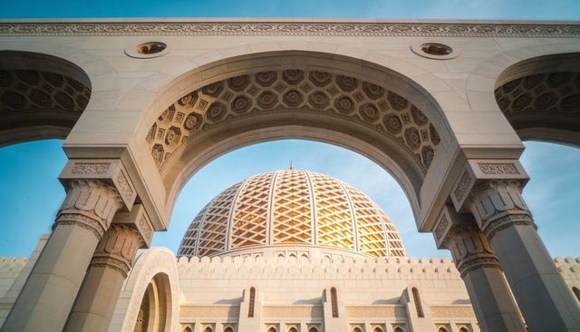 Sunlit geometric dome framed by ornate arches of grand islamic gateway