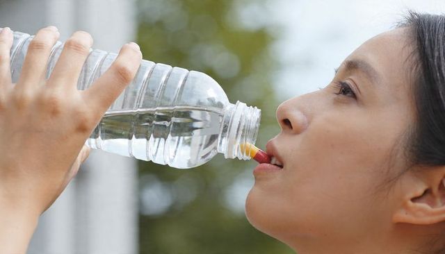 Asian woman drinking from clear plastic bottle with yellow nozzle closeup outdoors