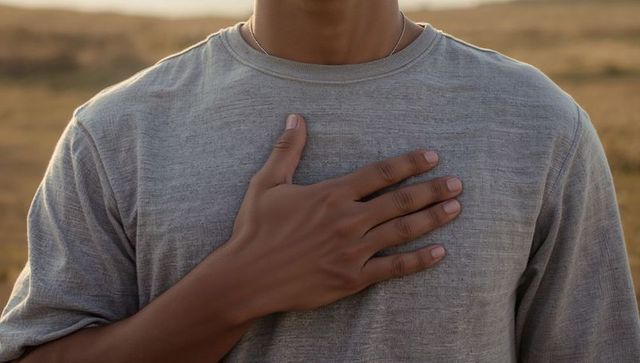 Man placing hand over chest in golden-hour field wearing gray t-shirt and necklace