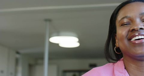 African woman laughing in pink blazer with gold hoop earrings close-up office portrait