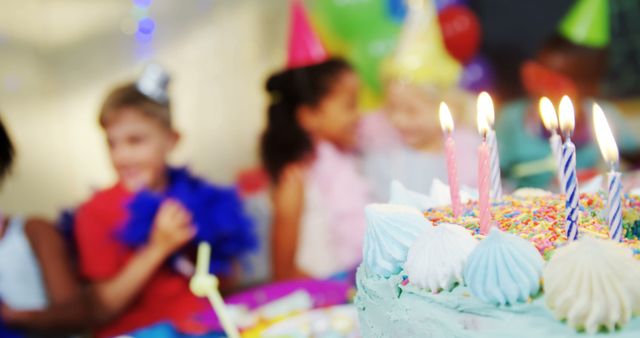 A birthday cake with lit candles is in focus, with diverse children wearing party hats blurred in the background, with copy space. Celebratory moments like these are cherished memories in a child's life.
