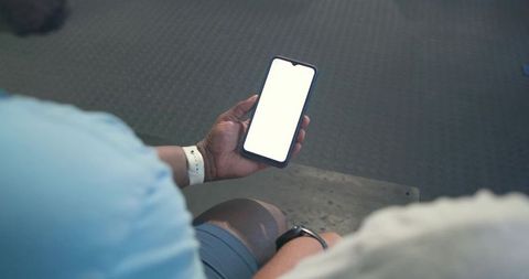 African american men checking smartphone on gym bench showing blank screen for app mockups