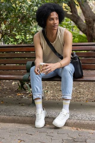 African american man sitting on park bench holding coffee cup casual contemplation in greenery