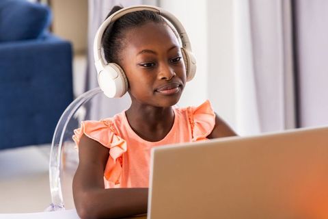 African girl studying online with headphones on laptop at home for remote learning focused