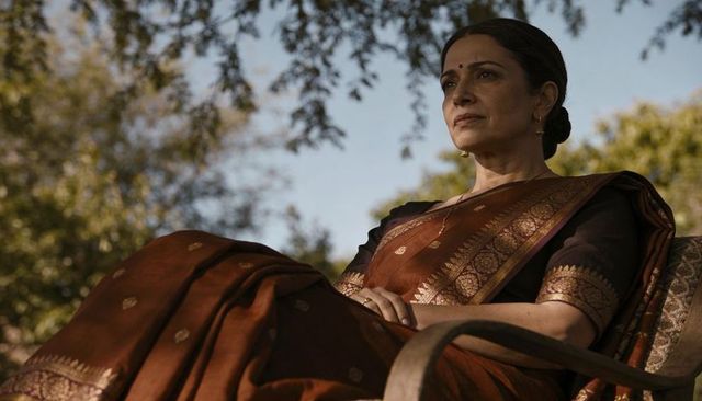 Sitting senior indian woman wearing maroon silk saree with gold jewelry, outdoor portrait