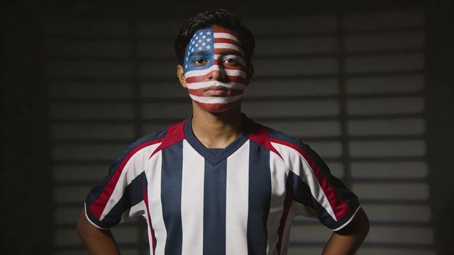 Young fan standing with us flag face paint wearing striped soccer jersey dramatic portrait