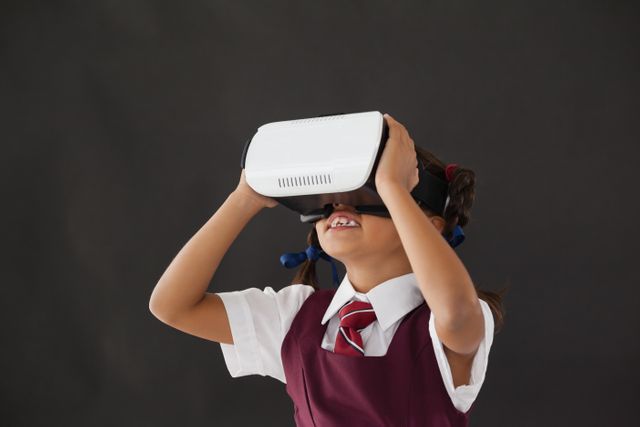 Schoolgirl using virtual reality headset against blackboard in classroom