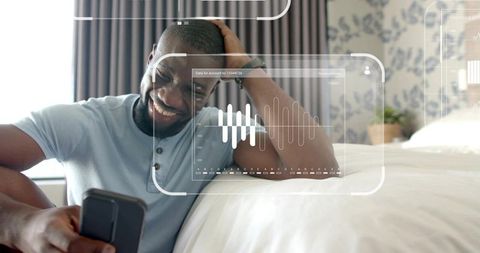 Smiling man wearing pale blue polo using smartphone in bedroom with digital ui overlays