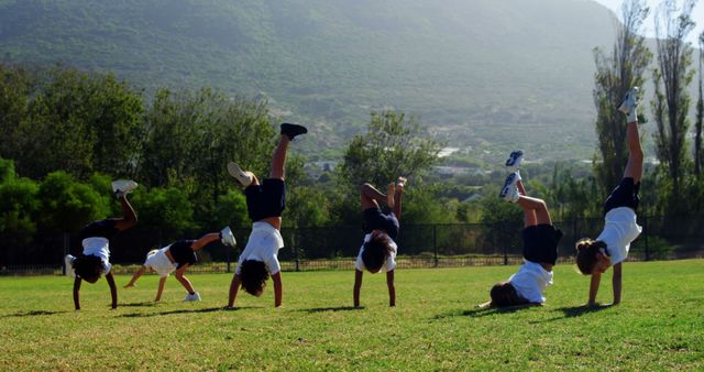 Children performing cartwheels in a sunny open field with greenery and mountains in the background. Perfect for promoting healthy and active lifestyles, childhood activities, outdoor fun, and fitness.