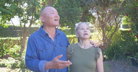 Senior couple exploring backyard garden while man pointing and guiding woman with optimism