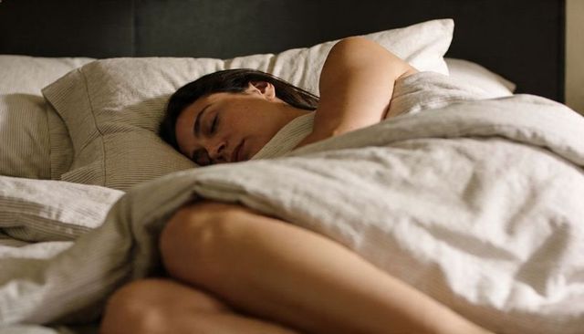Sleeping woman on side in neutral striped linen bedding, cozy bedroom rest and relaxation