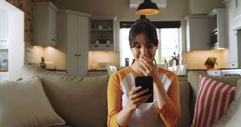 Young woman surprised by mobile phone in cozy living room