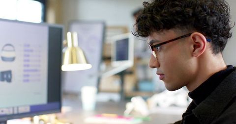 Focused young professional reviewing product UI on monitor in modern coworking workspace