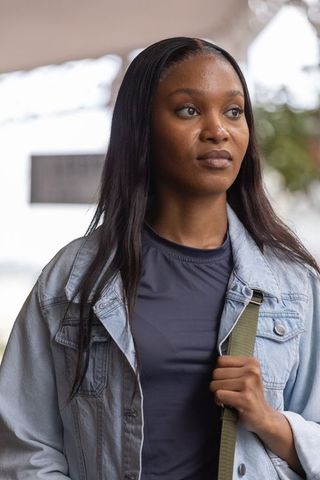 Young african woman standing under canopy wearing denim jacket holding green bag strap