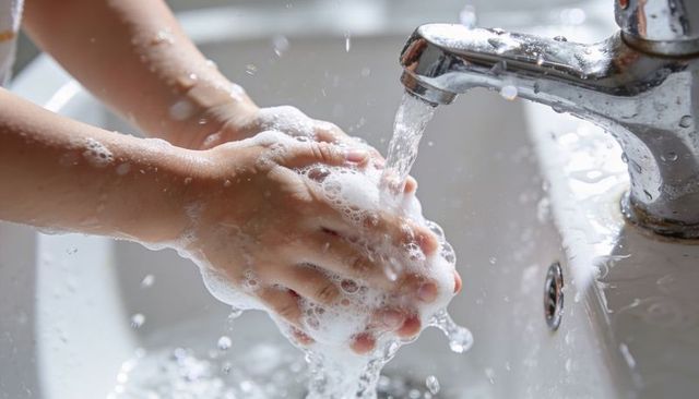 Toddler washing soapy hands under faucet with water splash closeup hygiene care for kids