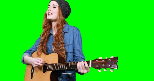 Female musician singing while playing guitar against green screen