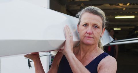 Senior Woman Carrying Rowing Boat in Boathouse