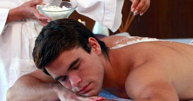 Handsome man getting a salt scrub treatment at the spa