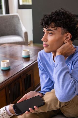 Thoughtful Young Man Relaxing with Smartphone Indoors