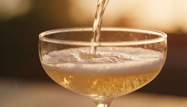 Golden champagne pour in coupe glass with foamy head and bubbles on outdoor sunset terrace