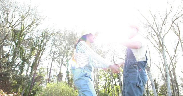 A young Caucasian couple is holding hands and spinning around joyfully in a sunlit park, with copy space. Their playful movement and the bright sunlight create a sense of happiness and freedom.