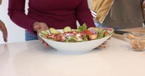 Diverse friends sharing fresh salad bowl on modern kitchen counter, teamwork cooking