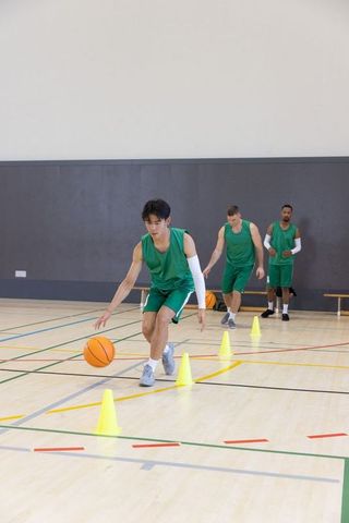 Diverse male basketball players dribbling through cone agility drill practicing teamwork