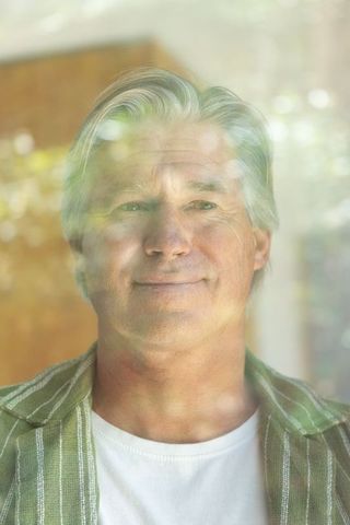 Senior man gazing through reflective window, contemplating life, serene home portrait
