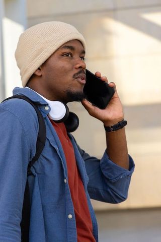Young african american man talking on smartphone while commuting, wearing beanie and headphones