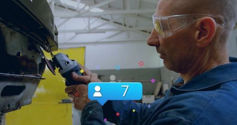 Mechanic grinding rusted car bumper in workshop wearing safety goggles using angle grinder