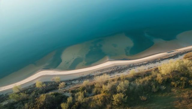 Aerial coastline at sunrise with curving sandbar, winding beach road and turquoise water