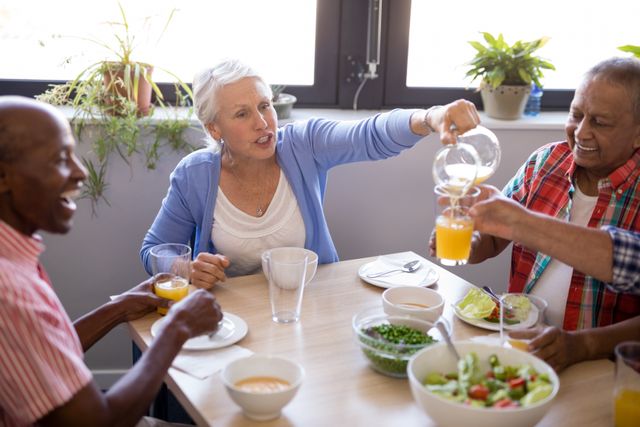 Senior woman talking while serving juice to friends at table in nursing home