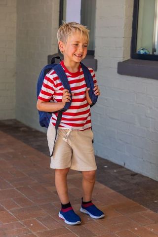 Smiling blond boy carrying backpack on porch, back-to-school casual lifestyle