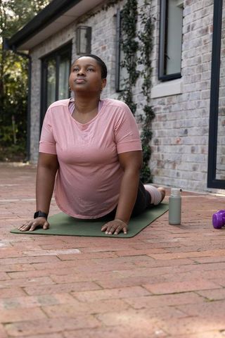 African american woman practicing yoga backbend on backyard brick patio in pink top