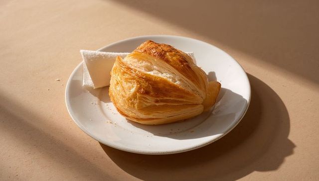 Golden laminated pastry basking in warm sunlight on white plate with napkin and crumbs